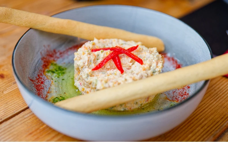 Une jolie petite assiette à bords hauts, bleu ciel, qui contient une spécialité culinaire espagnole présentée sous forme d'un petit médaillon