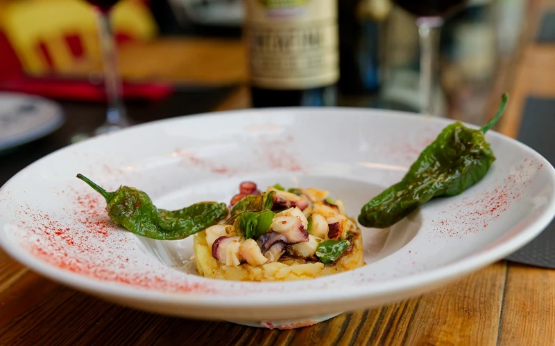 Assiette creuse accueillant une spécialité gastronomique espagnole avec du poulpe, des pimientos de padron