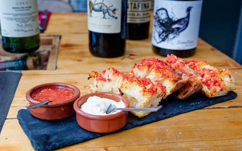 Spécialités espagnoles présentées sur une ardoise. Pan con tomate. Des tranches de pain grillé à la tomate, accompagnées de 2 raviers de sauce tomate et aïoli