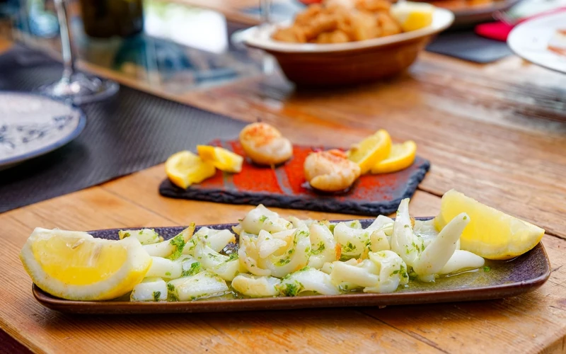 Petit plat allongé dans lequel est disposé une préparation à base de petits morceaux de poulpe et quartsde citron