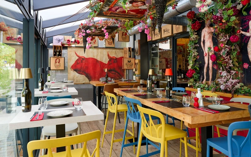 Terrasse d'un restaurant ibérique avec des tables en bois, des chaises jaunes et bleues, des fresques de taureaux et autres décorations espagnoles